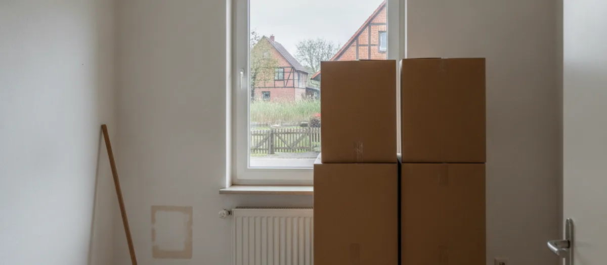Leere Wohnung mit gestapelten Umzugskartons vor einem Fenster kurz vor der Schlüsselübergabe